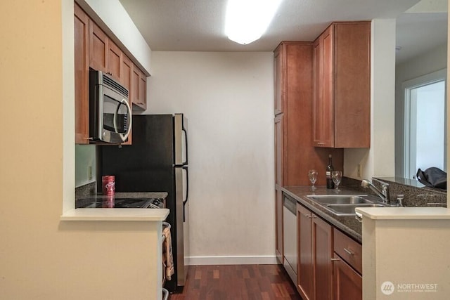 kitchen with stainless steel appliances, dark wood-type flooring, a peninsula, a sink, and brown cabinets