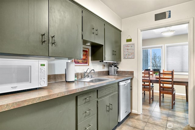 kitchen with stainless steel dishwasher, white microwave, light tile patterned flooring, a sink, and green cabinetry