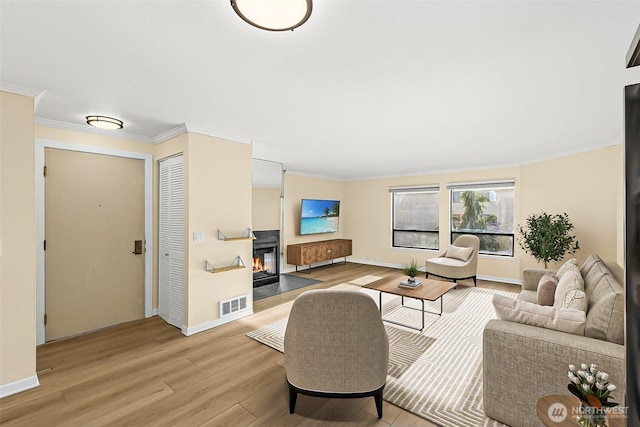 living area featuring wood finished floors, visible vents, baseboards, ornamental molding, and a glass covered fireplace