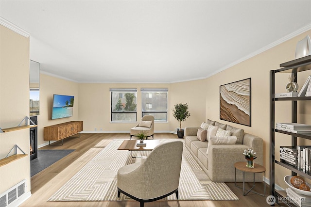 living room with ornamental molding, visible vents, baseboards, and wood finished floors