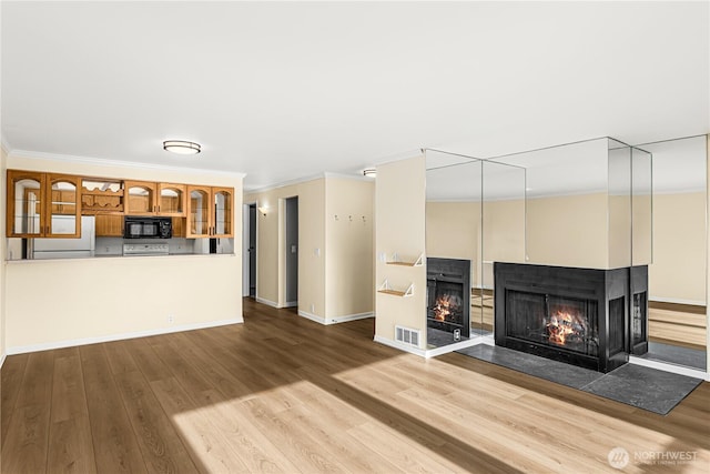 unfurnished living room featuring visible vents, ornamental molding, wood finished floors, and a multi sided fireplace