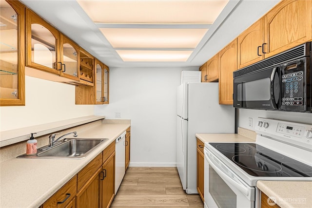 kitchen featuring light countertops, light wood-style floors, glass insert cabinets, a sink, and white appliances