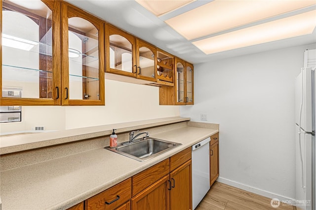 kitchen featuring glass insert cabinets, a sink, light wood-type flooring, white appliances, and baseboards