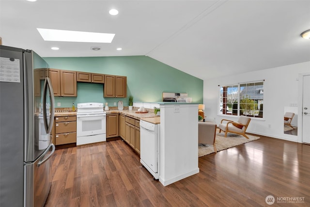 kitchen featuring a peninsula, white appliances, open floor plan, lofted ceiling with skylight, and dark wood finished floors