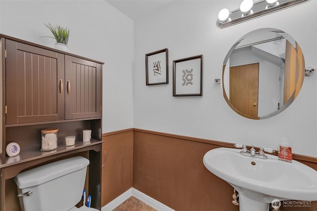 half bathroom with wainscoting, a sink, and toilet