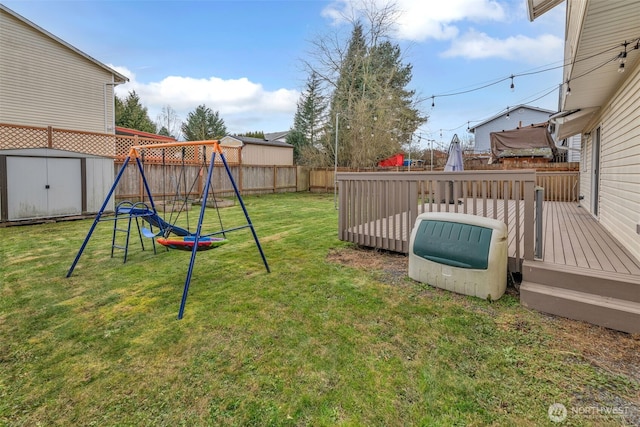 view of yard with a fenced backyard, an outbuilding, a storage unit, a wooden deck, and a playground