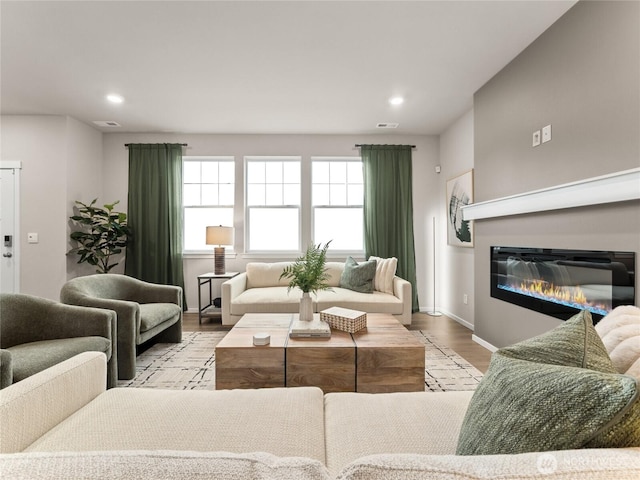 living area with recessed lighting, wood finished floors, visible vents, baseboards, and a glass covered fireplace