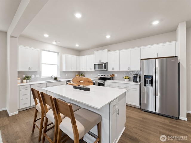 kitchen with a kitchen island, a breakfast bar area, appliances with stainless steel finishes, wood finished floors, and a sink