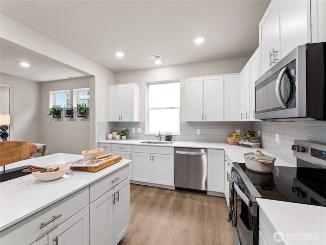 kitchen with a sink, white cabinets, light countertops, appliances with stainless steel finishes, and a wealth of natural light