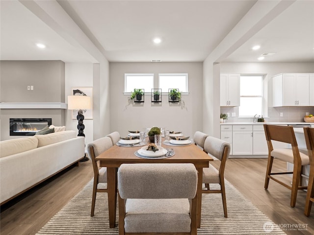 dining area with a glass covered fireplace, light wood finished floors, and recessed lighting