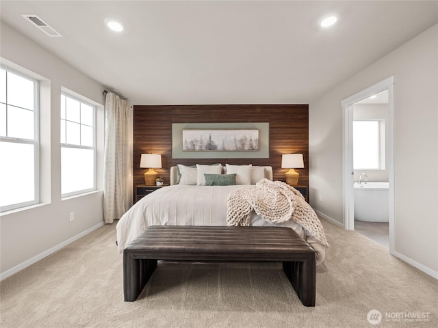 bedroom with an accent wall, multiple windows, visible vents, and light colored carpet