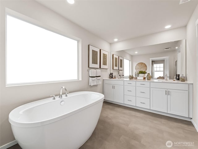 bathroom with recessed lighting, a freestanding bath, a sink, and double vanity