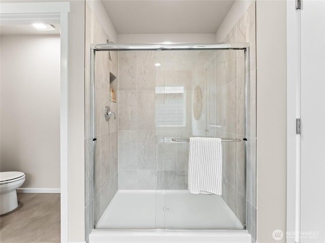 bathroom featuring a shower stall, toilet, and baseboards