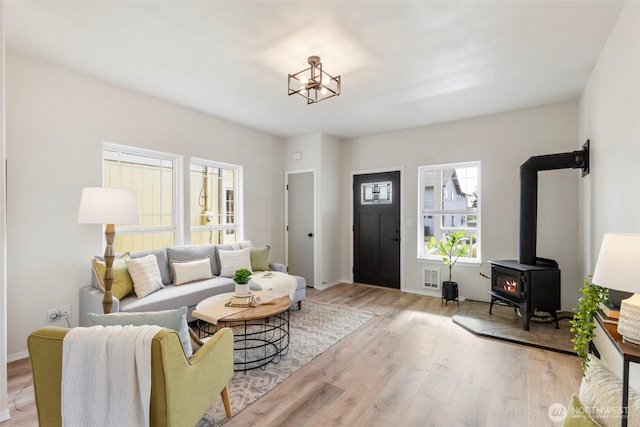 living room with light wood-type flooring, a wood stove, baseboards, and visible vents