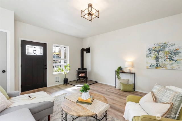 living room featuring light wood-style floors, a wood stove, visible vents, and baseboards