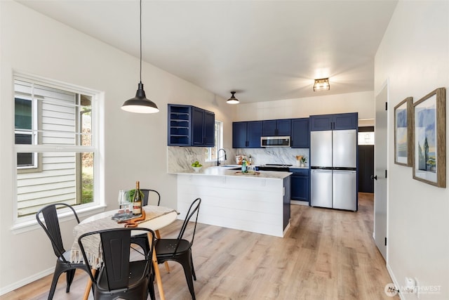 kitchen with a peninsula, stainless steel appliances, light countertops, blue cabinetry, and backsplash