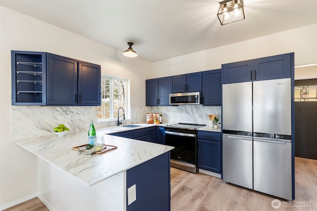 kitchen featuring appliances with stainless steel finishes, blue cabinets, a sink, and a peninsula