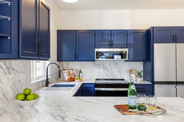 kitchen featuring a sink, blue cabinetry, appliances with stainless steel finishes, decorative backsplash, and light stone countertops