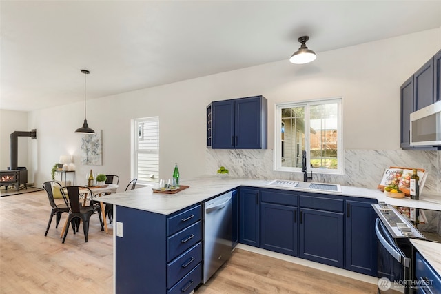 kitchen featuring blue cabinetry, appliances with stainless steel finishes, a peninsula, and a sink