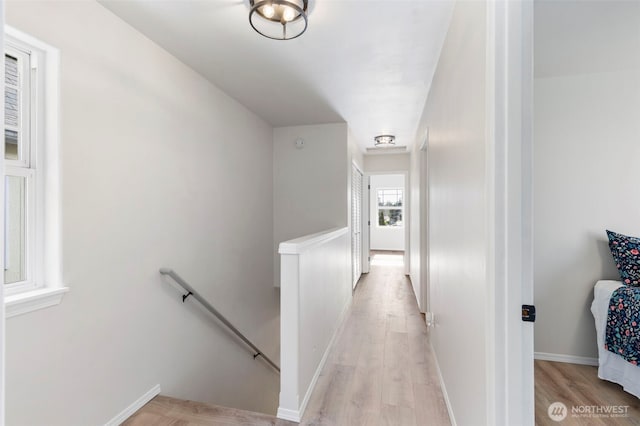 corridor featuring light wood-style flooring, an upstairs landing, and baseboards