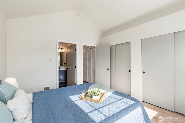 bedroom with high vaulted ceiling, two closets, visible vents, light wood-type flooring, and ensuite bath