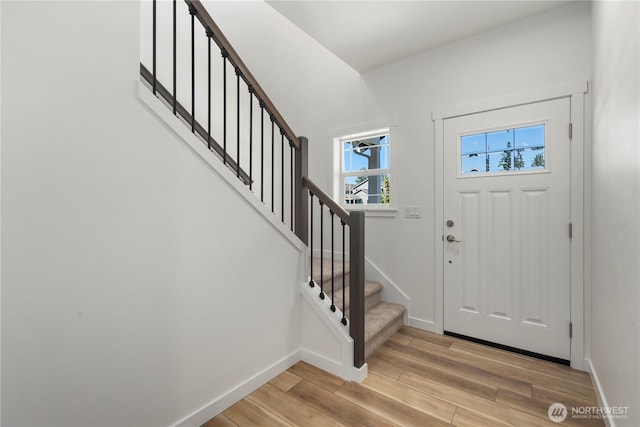 foyer entrance with stairway, light wood-style flooring, and baseboards