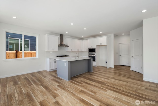 kitchen with white cabinets, wall chimney range hood, stainless steel appliances, and a sink