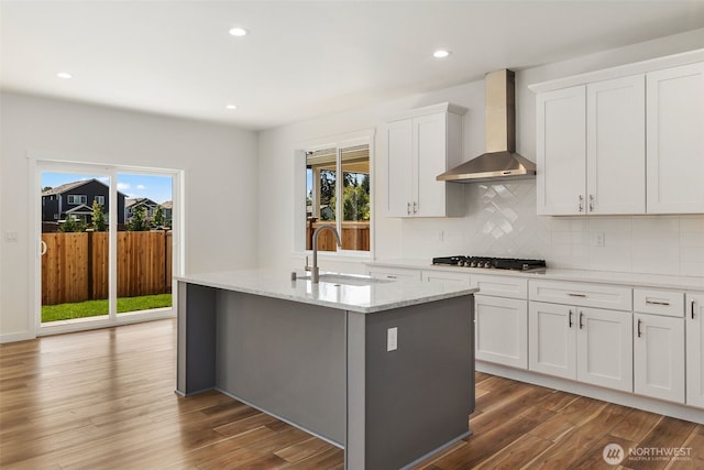 kitchen with stainless steel gas stovetop, decorative backsplash, a sink, wood finished floors, and wall chimney exhaust hood