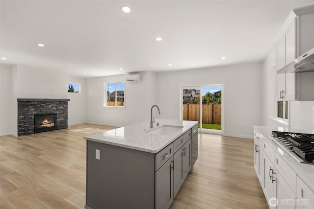 kitchen with wall chimney exhaust hood, appliances with stainless steel finishes, gray cabinets, light wood-style floors, and a sink