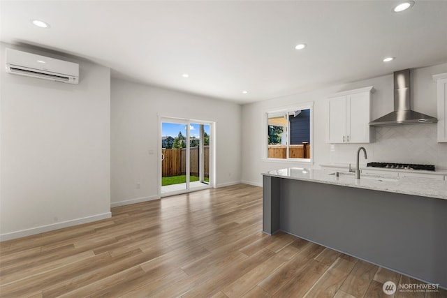 kitchen with wall chimney exhaust hood, a wall mounted air conditioner, backsplash, and light wood-style flooring