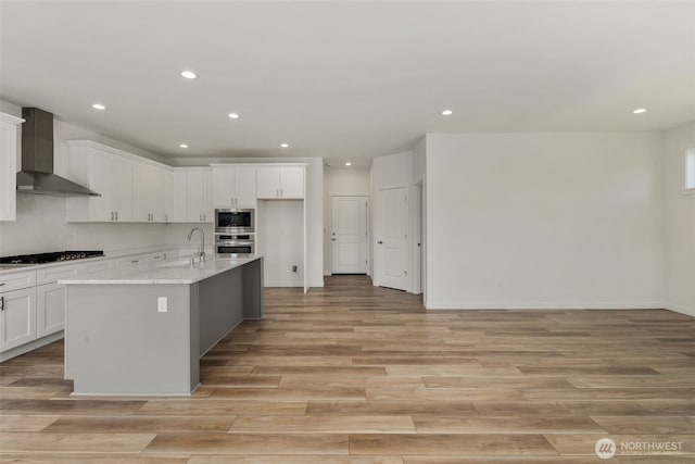 kitchen with wall chimney range hood, tasteful backsplash, stainless steel microwave, and light wood-style floors