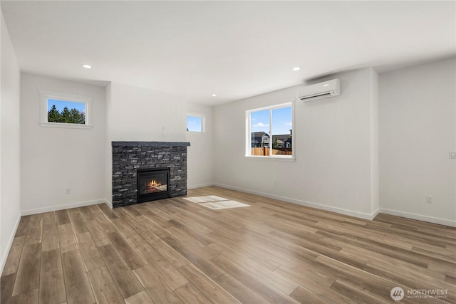 unfurnished living room featuring baseboards, a wall mounted air conditioner, a fireplace, and light wood-style floors