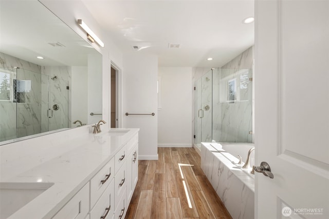 bathroom with wood finished floors, visible vents, a sink, a marble finish shower, and double vanity