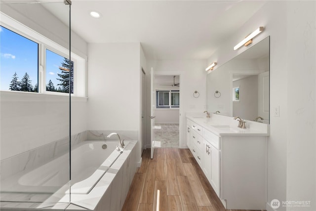 full bath featuring a bath, double vanity, a sink, and wood finished floors