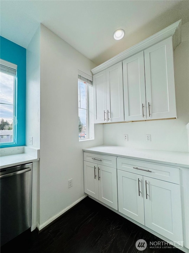 kitchen with light countertops, dark wood-type flooring, white cabinets, dishwasher, and baseboards