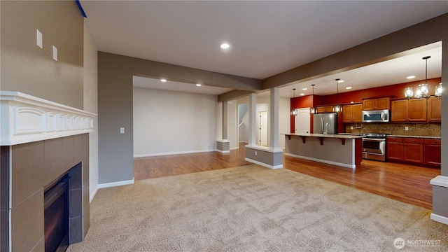 unfurnished living room featuring baseboards, a tiled fireplace, carpet floors, a chandelier, and recessed lighting