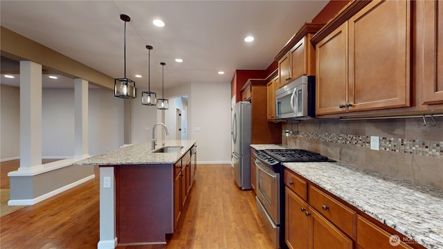 kitchen with tasteful backsplash, an island with sink, appliances with stainless steel finishes, light wood-type flooring, and a sink