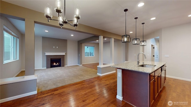 kitchen featuring an island with sink, light stone counters, hardwood / wood-style floors, a sink, and recessed lighting