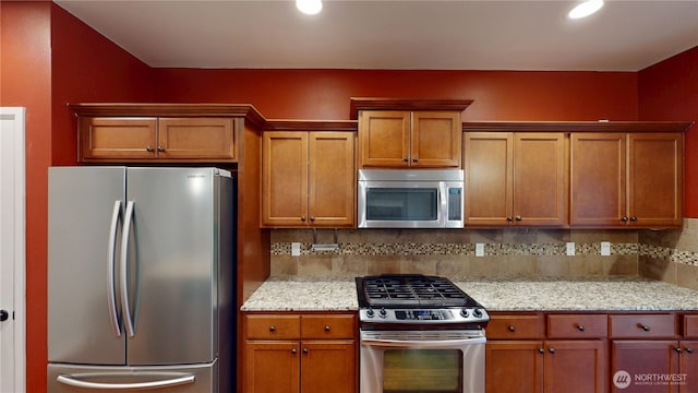 kitchen with appliances with stainless steel finishes, brown cabinetry, light stone countertops, and decorative backsplash