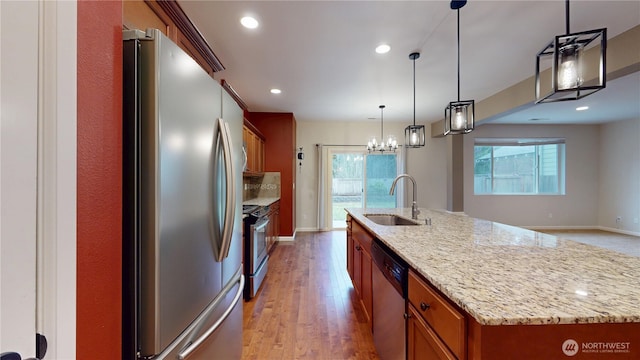 kitchen featuring light wood-style flooring, stainless steel appliances, a spacious island, a sink, and brown cabinets