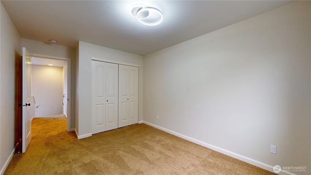 unfurnished bedroom featuring baseboards, a closet, and light colored carpet