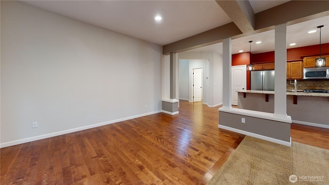 unfurnished living room with hardwood / wood-style floors, recessed lighting, beam ceiling, and baseboards