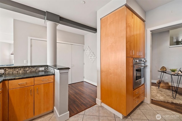 kitchen with dark countertops, light tile patterned floors, brown cabinets, and oven