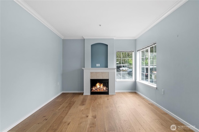 unfurnished living room with light wood finished floors, a lit fireplace, baseboards, and ornamental molding