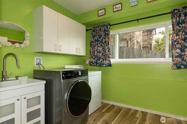 laundry room featuring a sink, wood finished floors, baseboards, cabinet space, and washer and clothes dryer