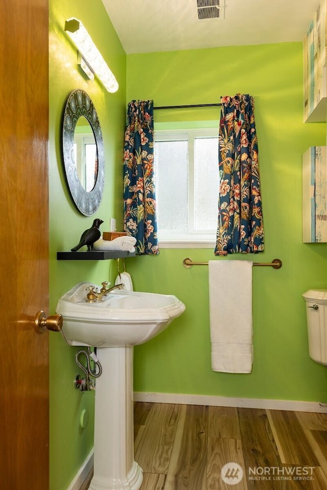 half bathroom featuring wood finished floors, visible vents, and baseboards