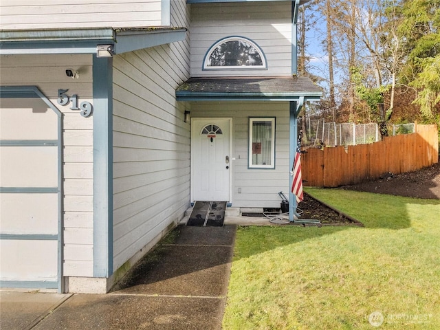 entrance to property featuring an attached garage, a shingled roof, fence, and a lawn