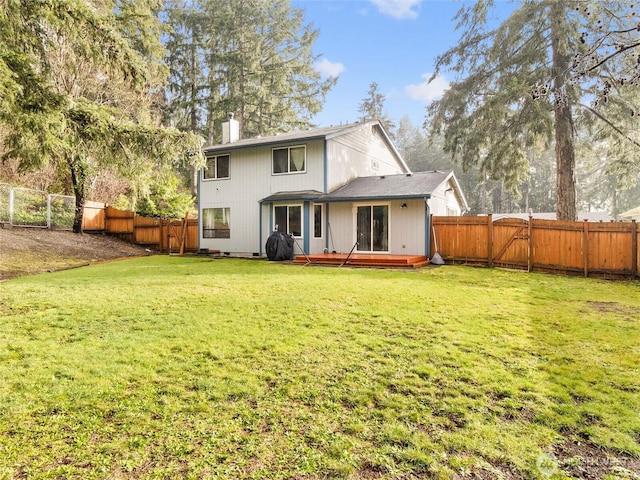 back of house featuring a gate, a fenced backyard, a yard, and a chimney