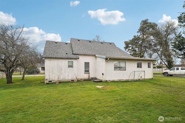 back of property featuring a shingled roof and a yard