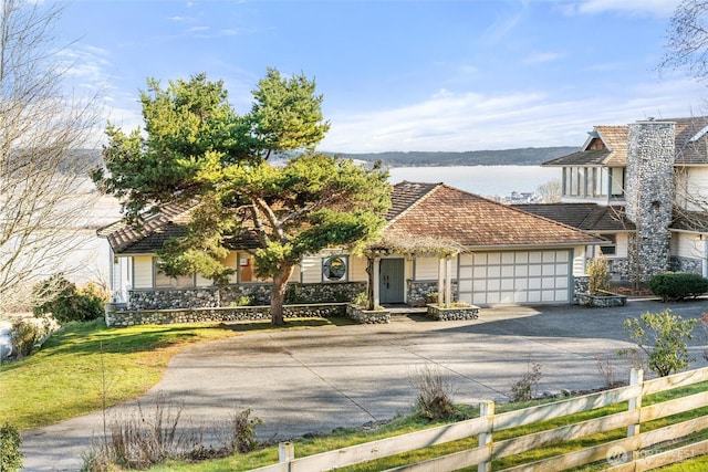 view of front of house with a fenced front yard, a garage, a water view, driveway, and stone siding